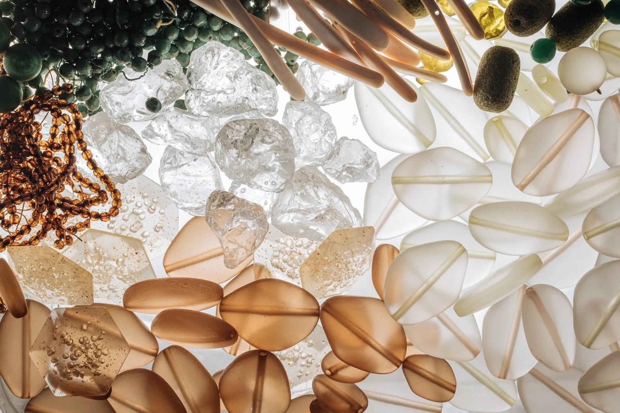 Un ensemble de divers objets décoratifs en verre, perles, pierres et éléments translucides de différentes formes et couleurs, suspendus ou dispersés.