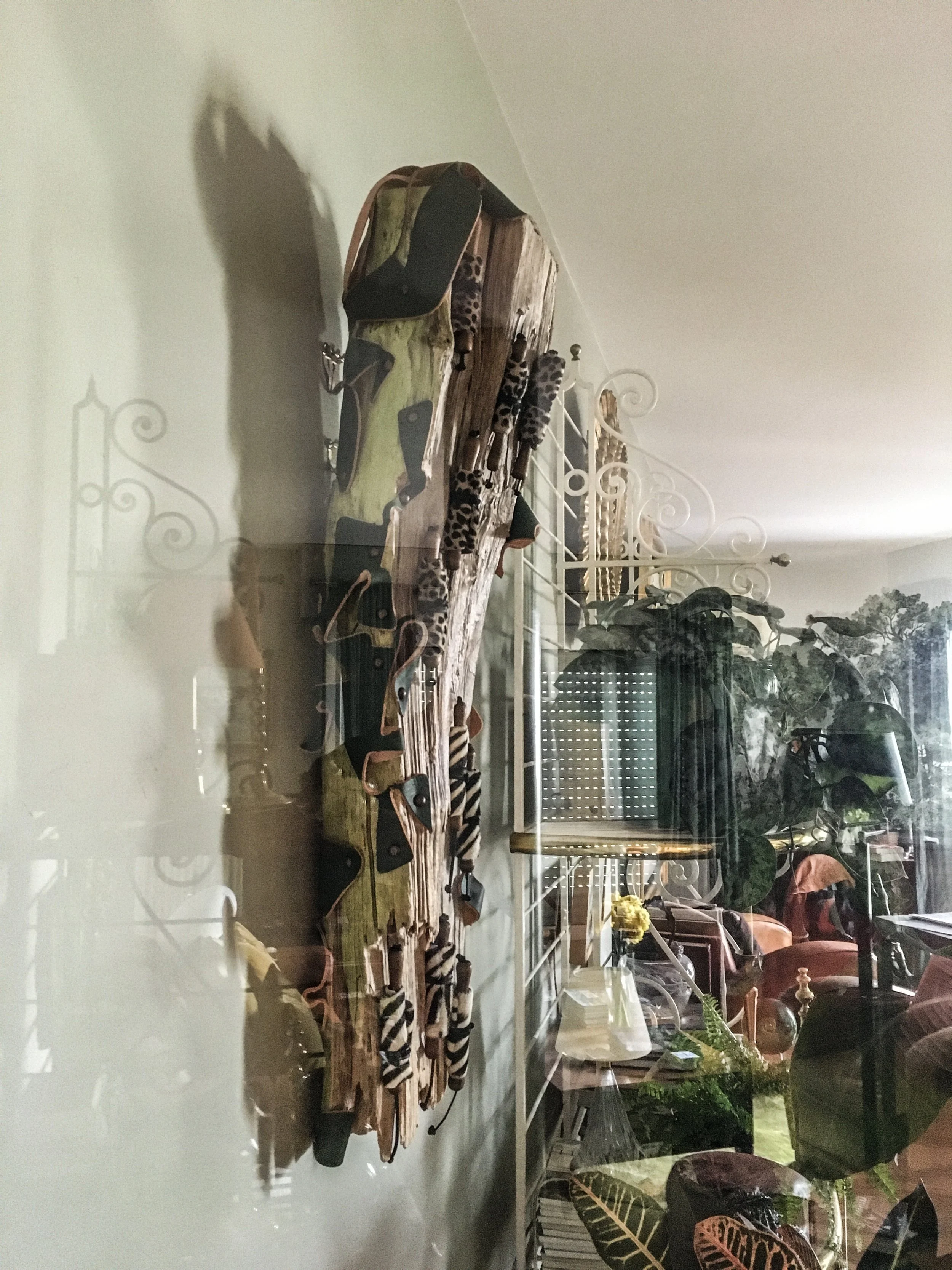 Une collection de sandales à talons hauts avec des motifs animaliers, exposées sur une planche en bois, visible à travers une vitre dans un intérieur décoré avec des meubles et des plantes.