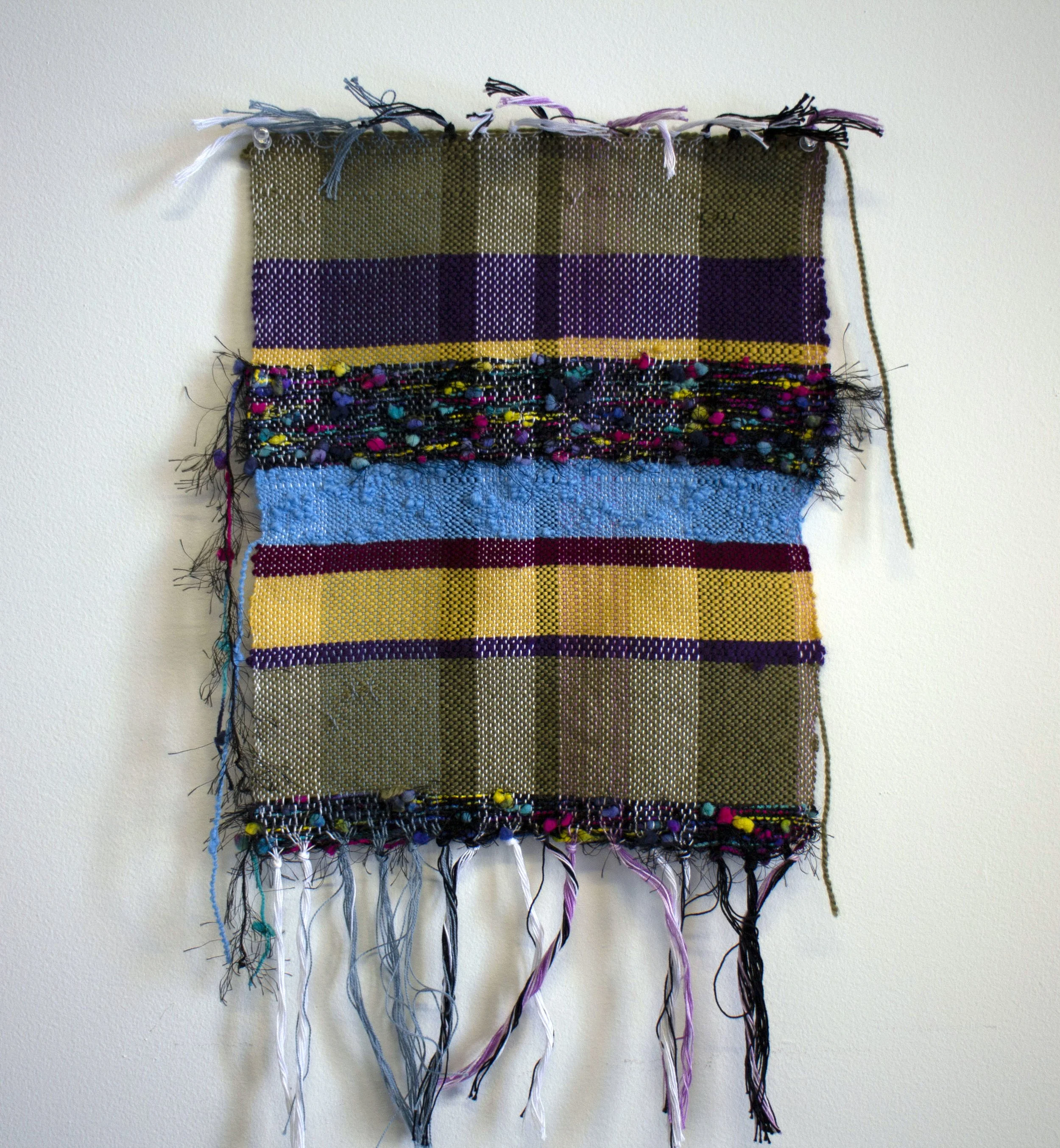 Woven rectangle with olive, mustard, blue and purple fibers.