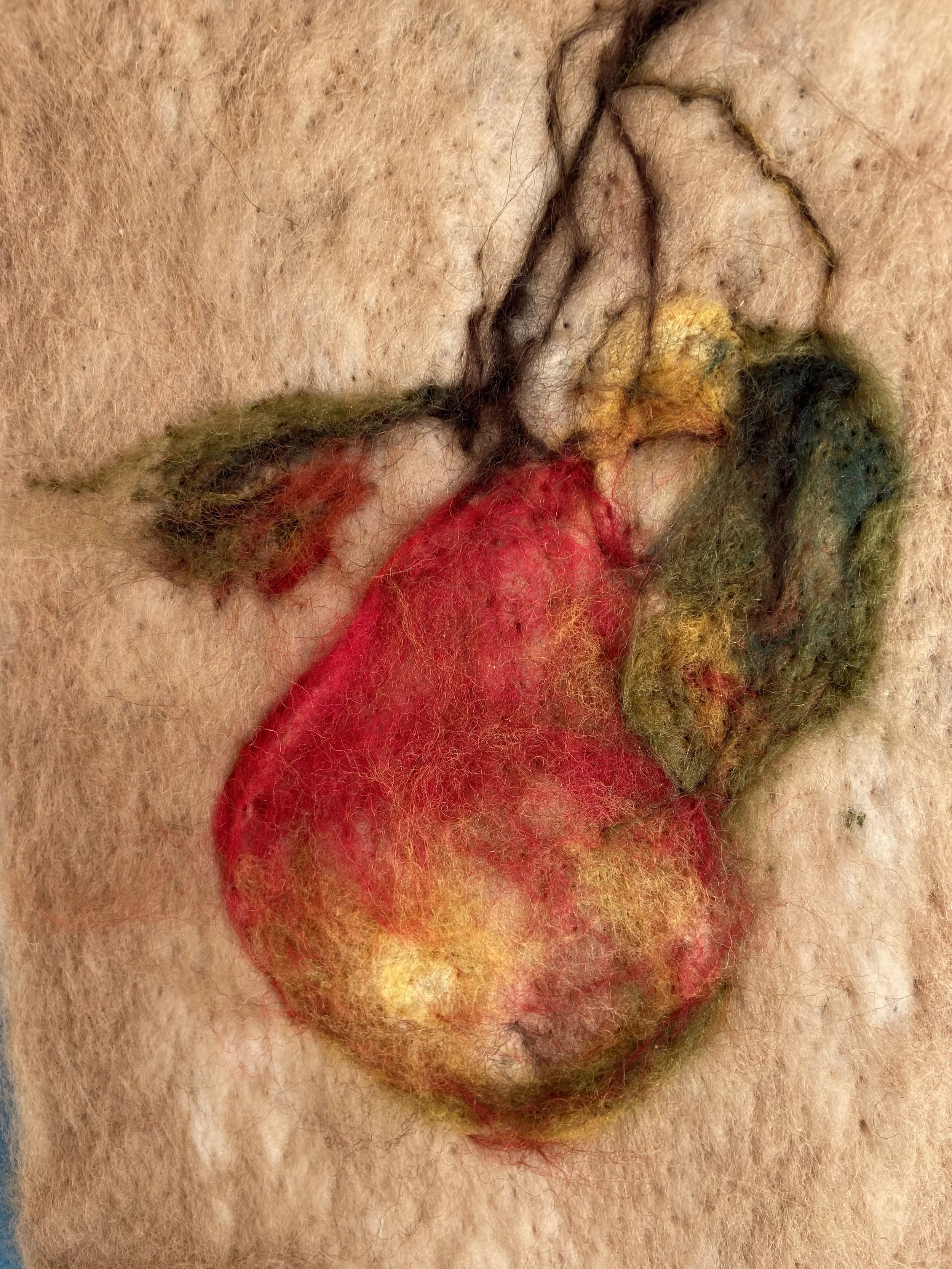 Needle felted wool fruit on a branch in cream, red, and green.