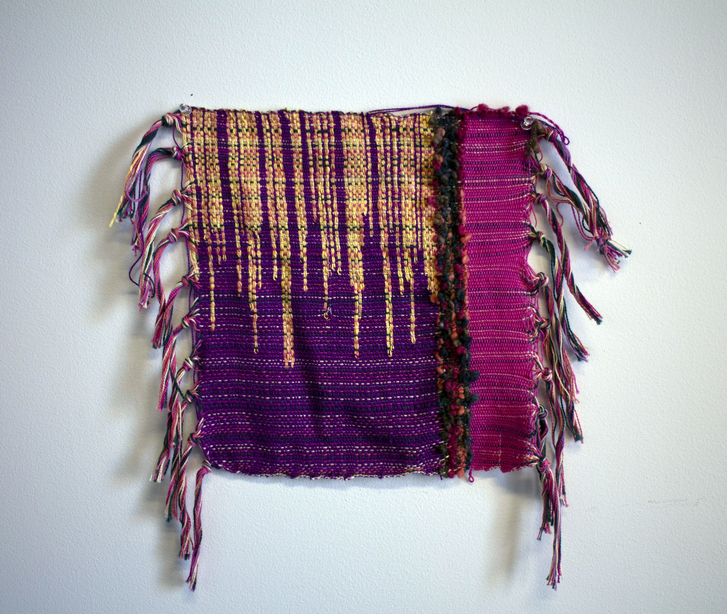 Woven rectangle with purple, gold, hot pink, and black fibers.