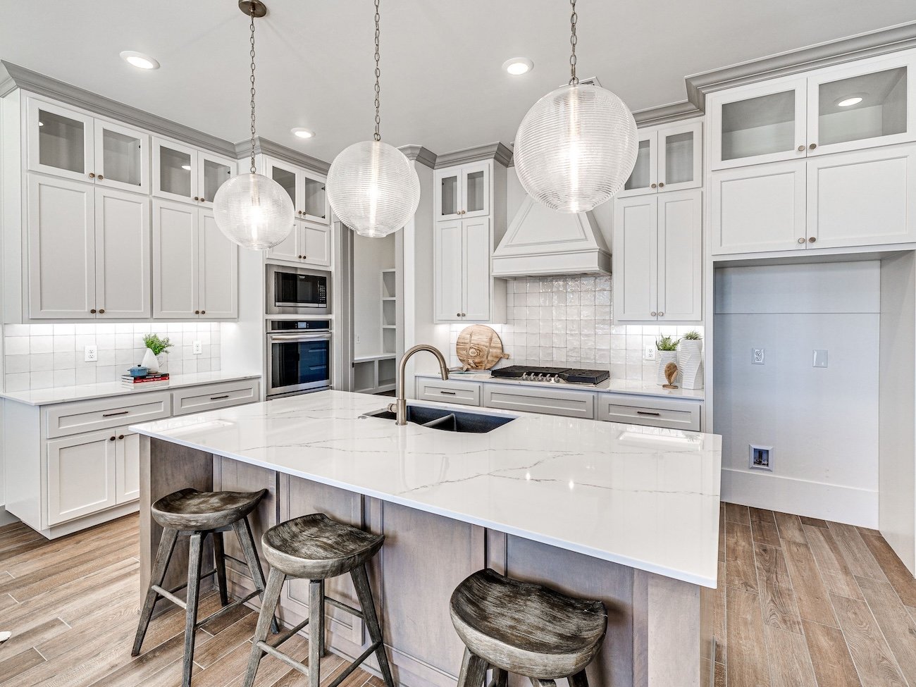 Modern kitchen with white cabinetry, marble island countertop, three globe pendant lights, stainless steel appliances, and wooden bar stools.
