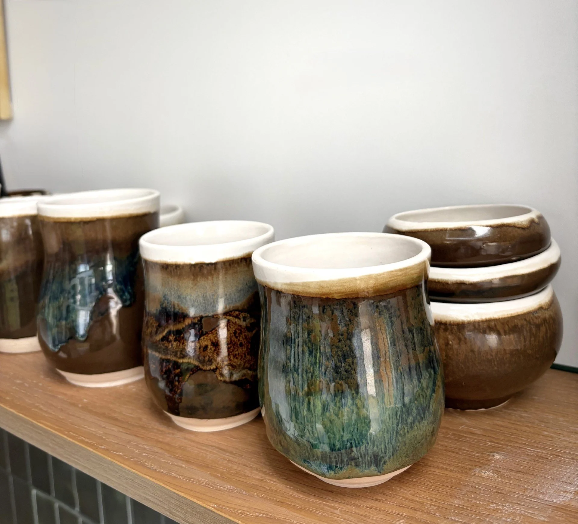 Collection of handmade unique ceramic pots with glazed, earthy tones and textured surfaces, arranged on a wooden shelf.