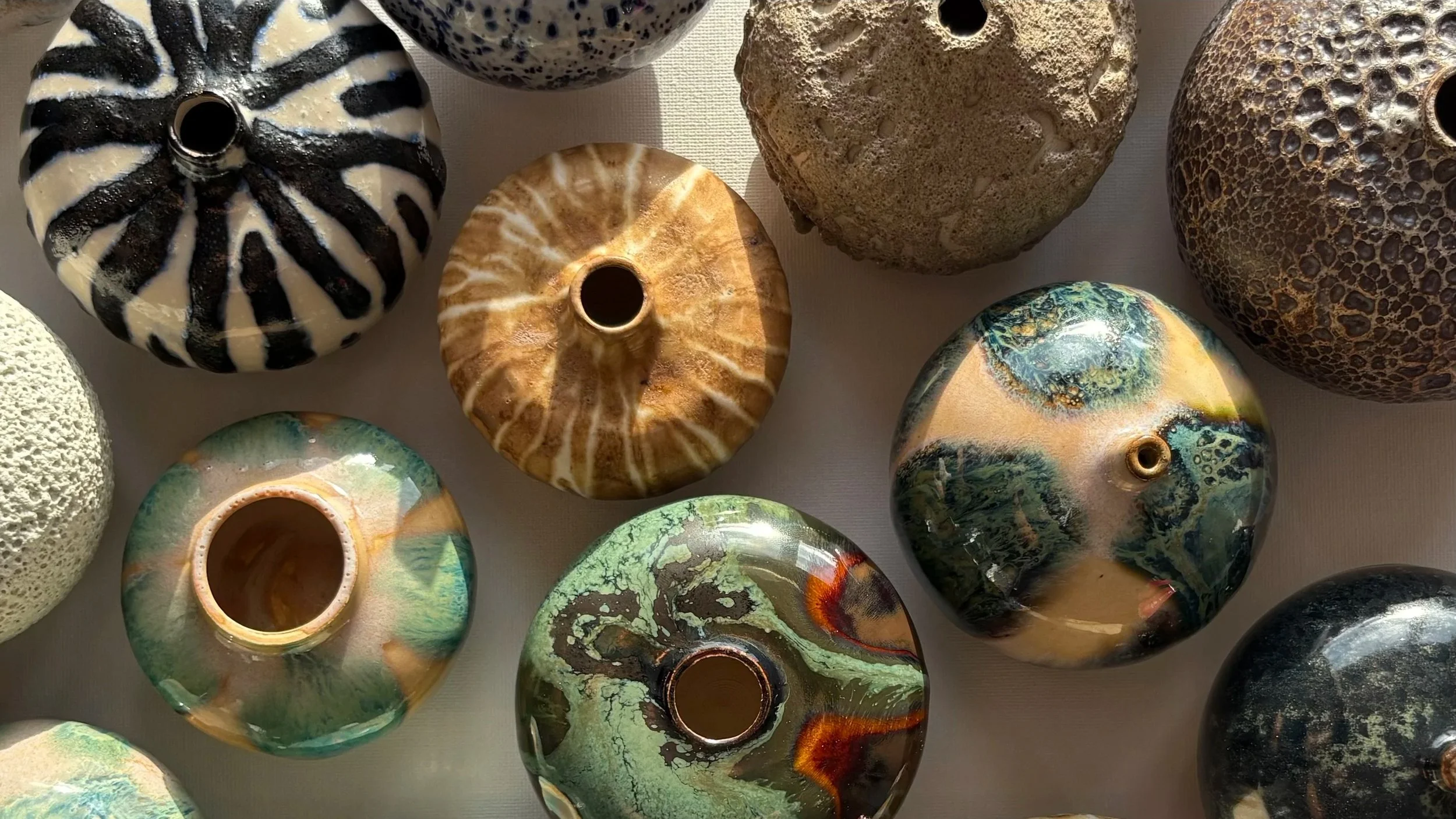 A collection of decorative glass vases with various patterns and colors, including black and white zebra stripes, brown and white streaks, green and brown marbled, and textured surfaces in neutral tones.