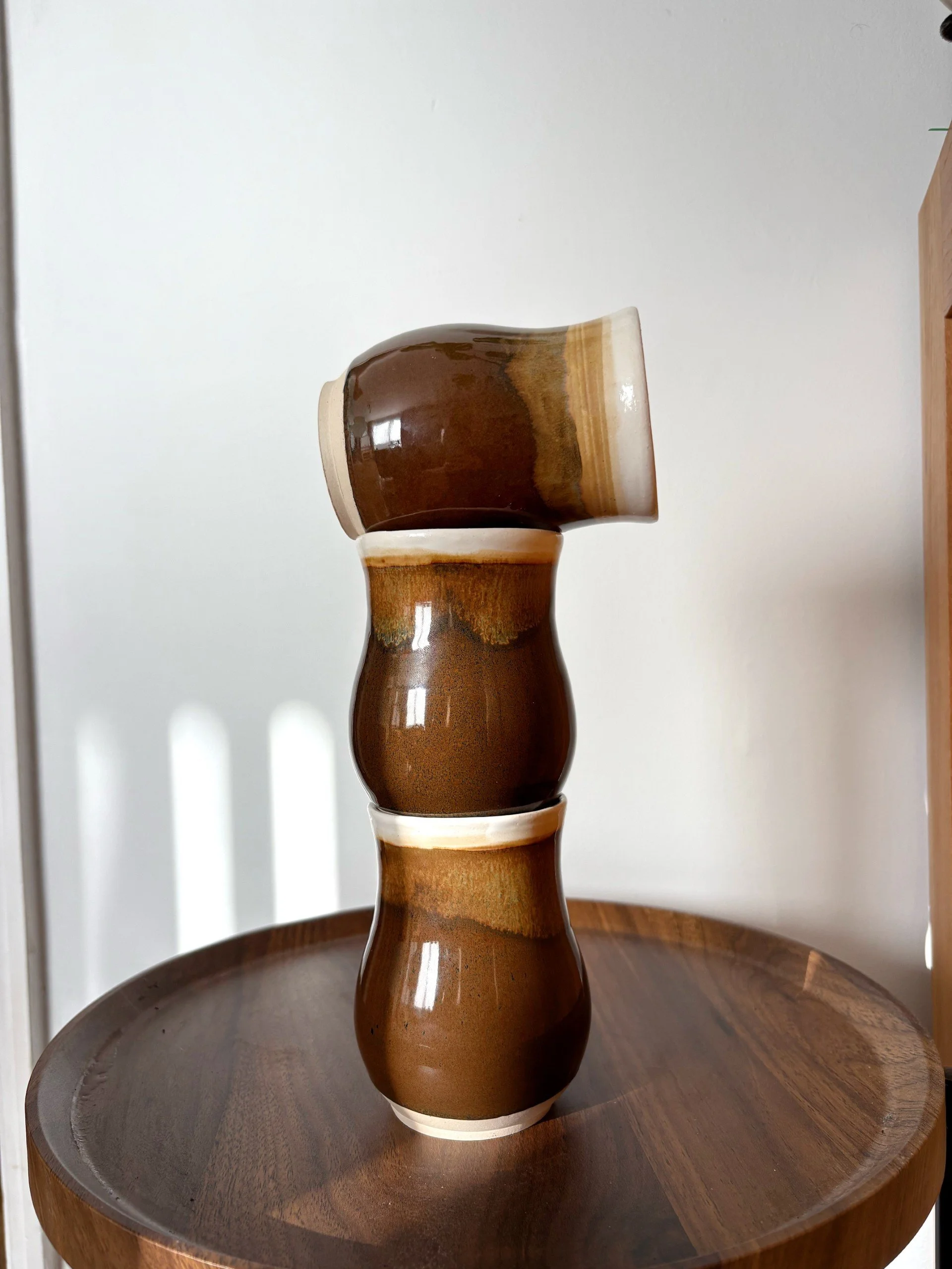 Stacked brown ceramic cups with cream-colored rims on a wooden surface.