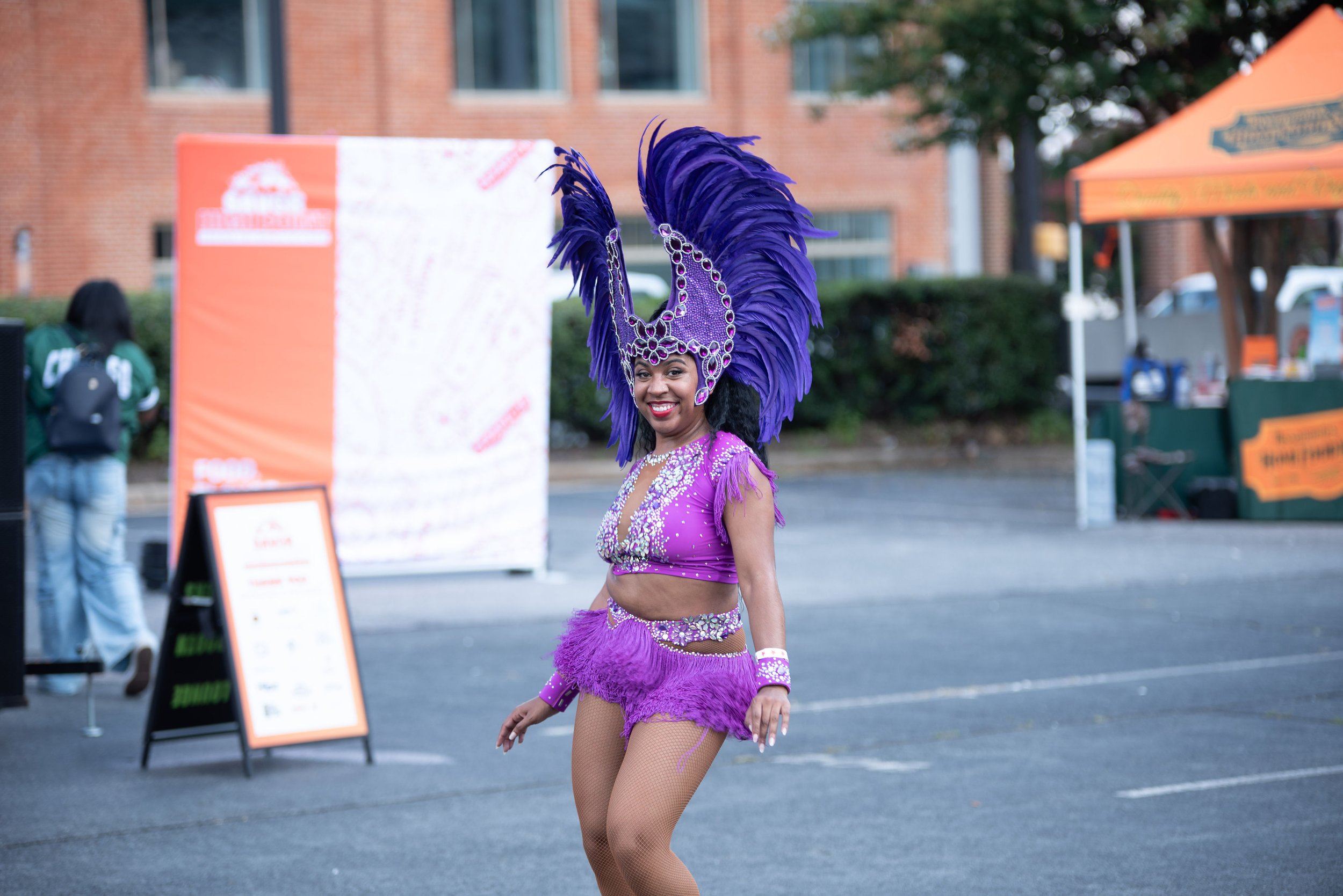 Woman in purple carnival costume with feathers smiling outdoors.