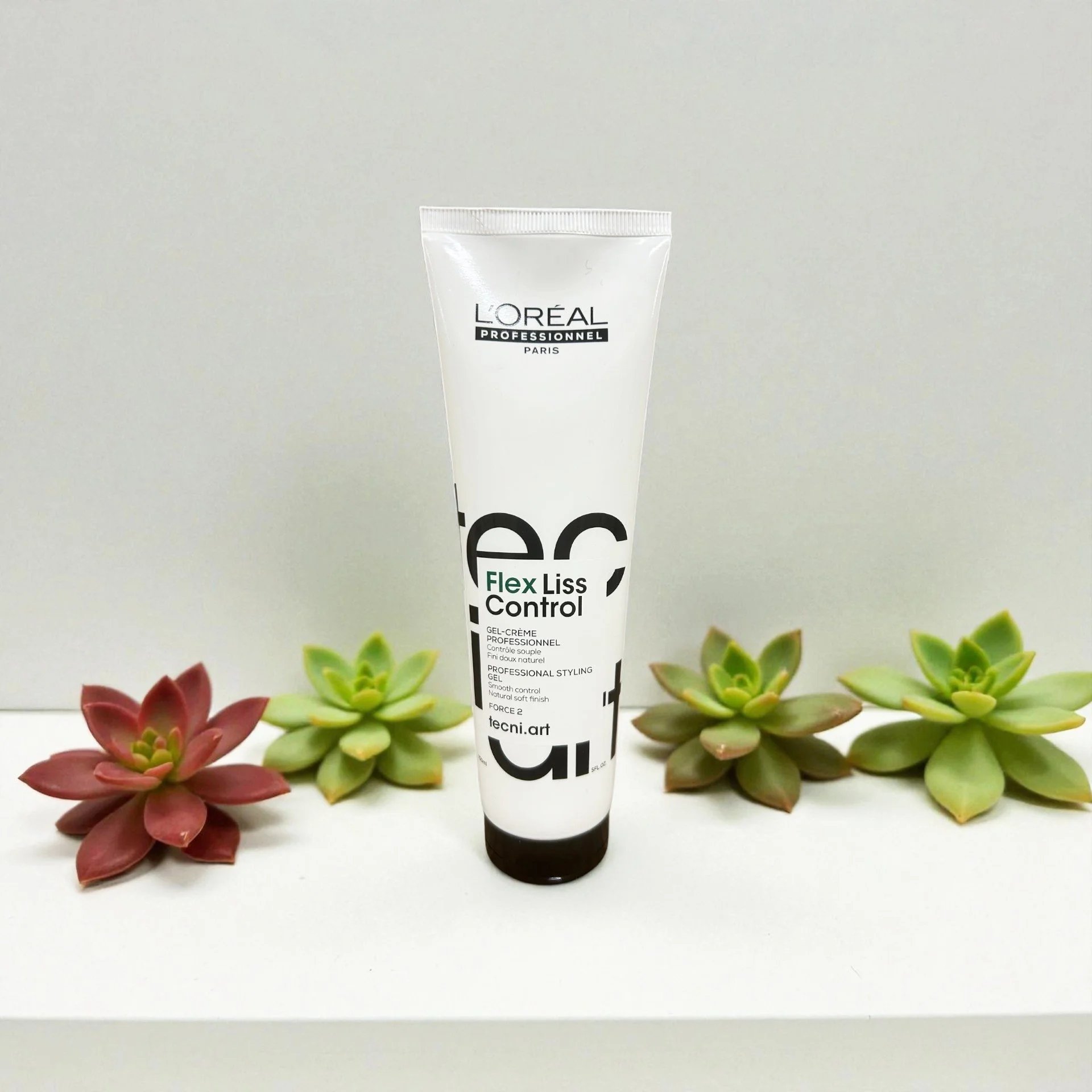 A tube of L'Oréal Professionnel Flex Liss Control gel cream on a white surface, surrounded by four succulent plants.