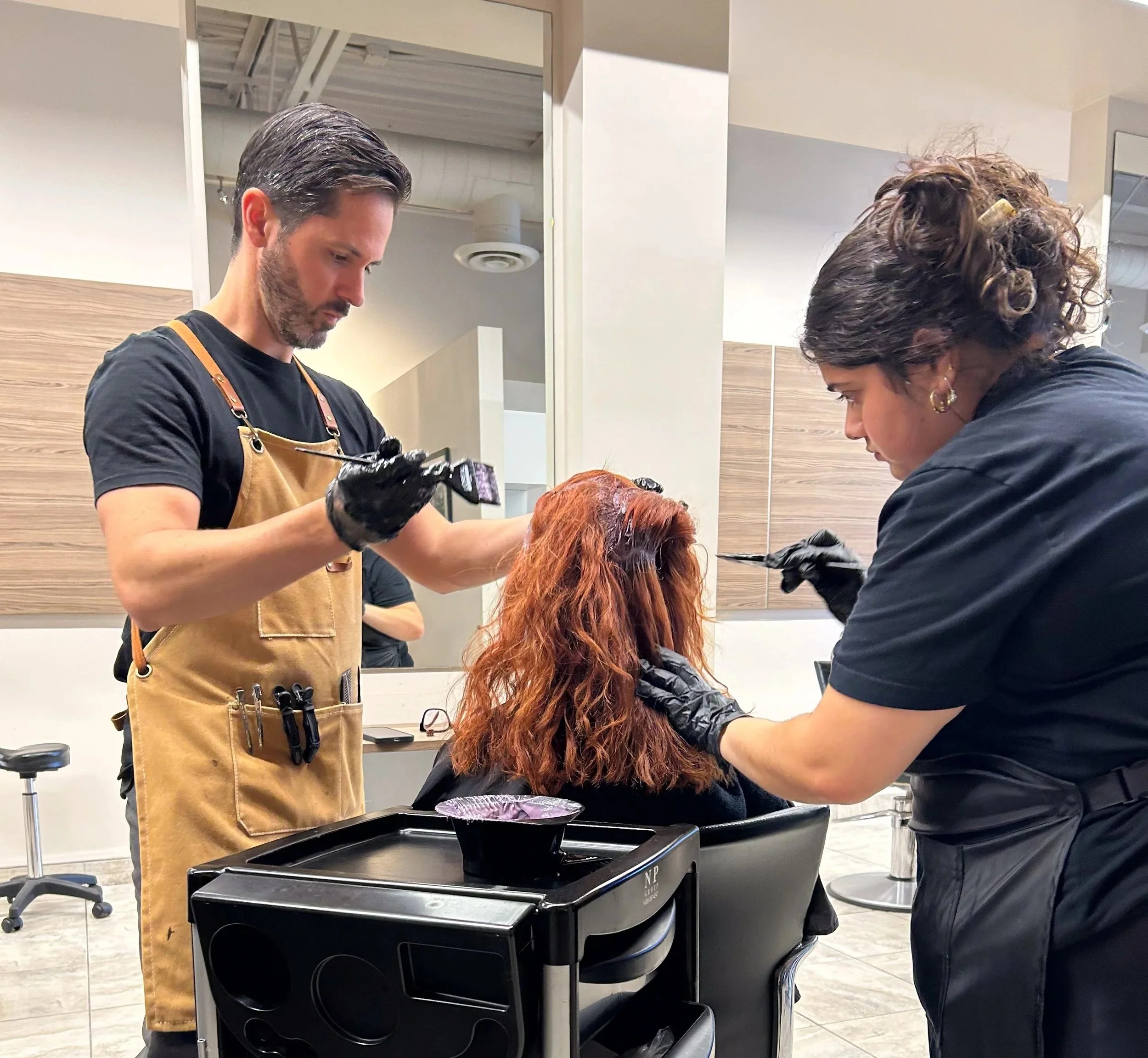 Hairdressers applying hair color to a woman in a salon.