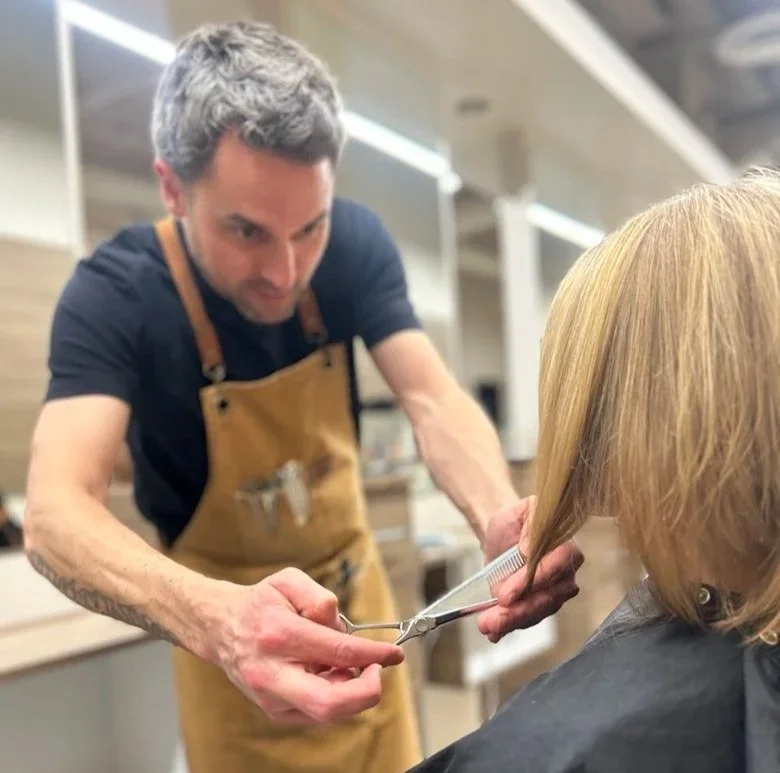 A hairstylist cutting a woman's hair with scissors in a salon.