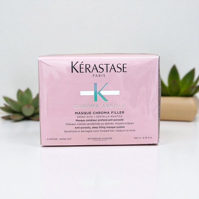 Pink box of Kérastase Chroma Absolu Masque Chroma Filler hair treatment with green succulent plants in the background.