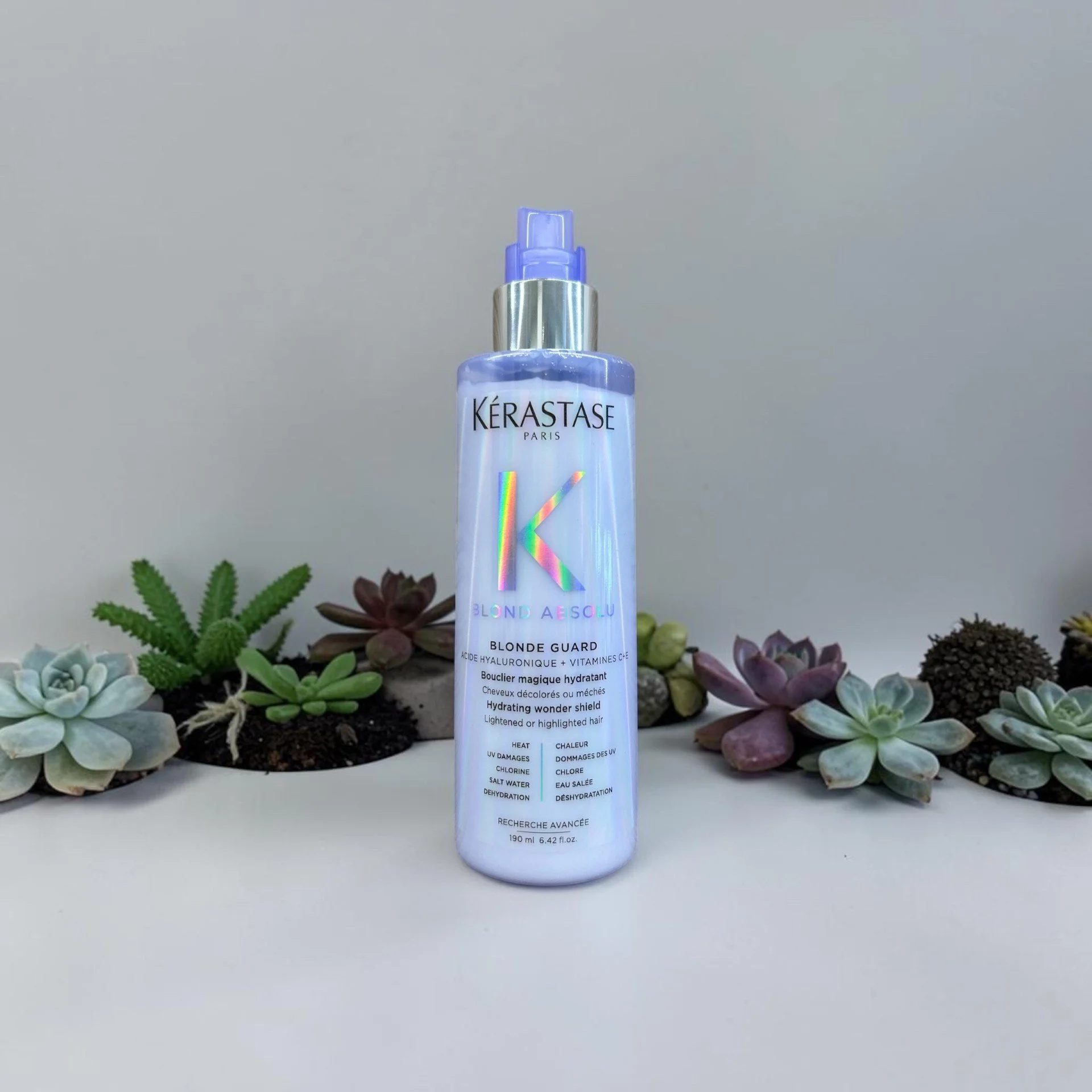 A bottle of Kérastase Blond Guard hair care product surrounded by assorted succulents.