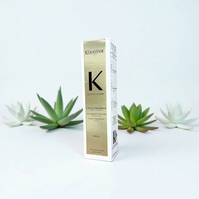 A tall white box of Kérastase Elixir Ultime hair product with succulent plants around it against a light background.