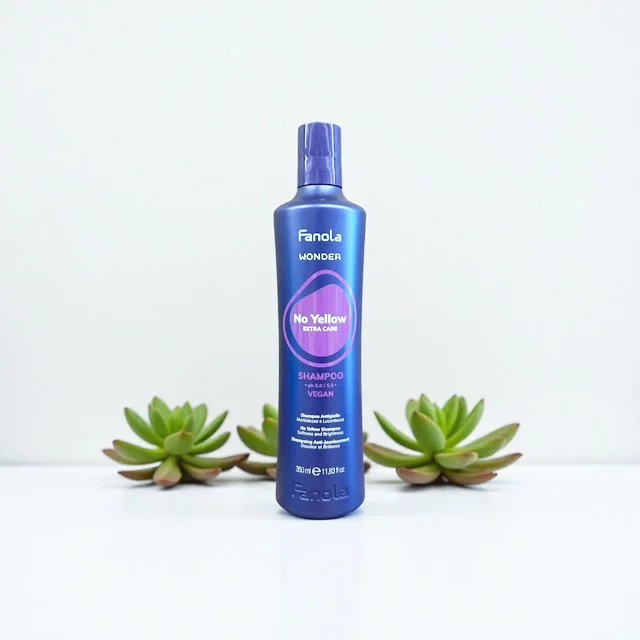 Blue bottle of Fanola Wonder No Yellow shampoo with succulents in the background on a white surface.