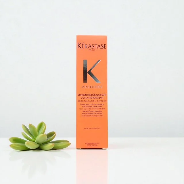 A bottle of Kérastase Paris Premier decalcifying conditioner with a succulent plant beside it on a white surface.