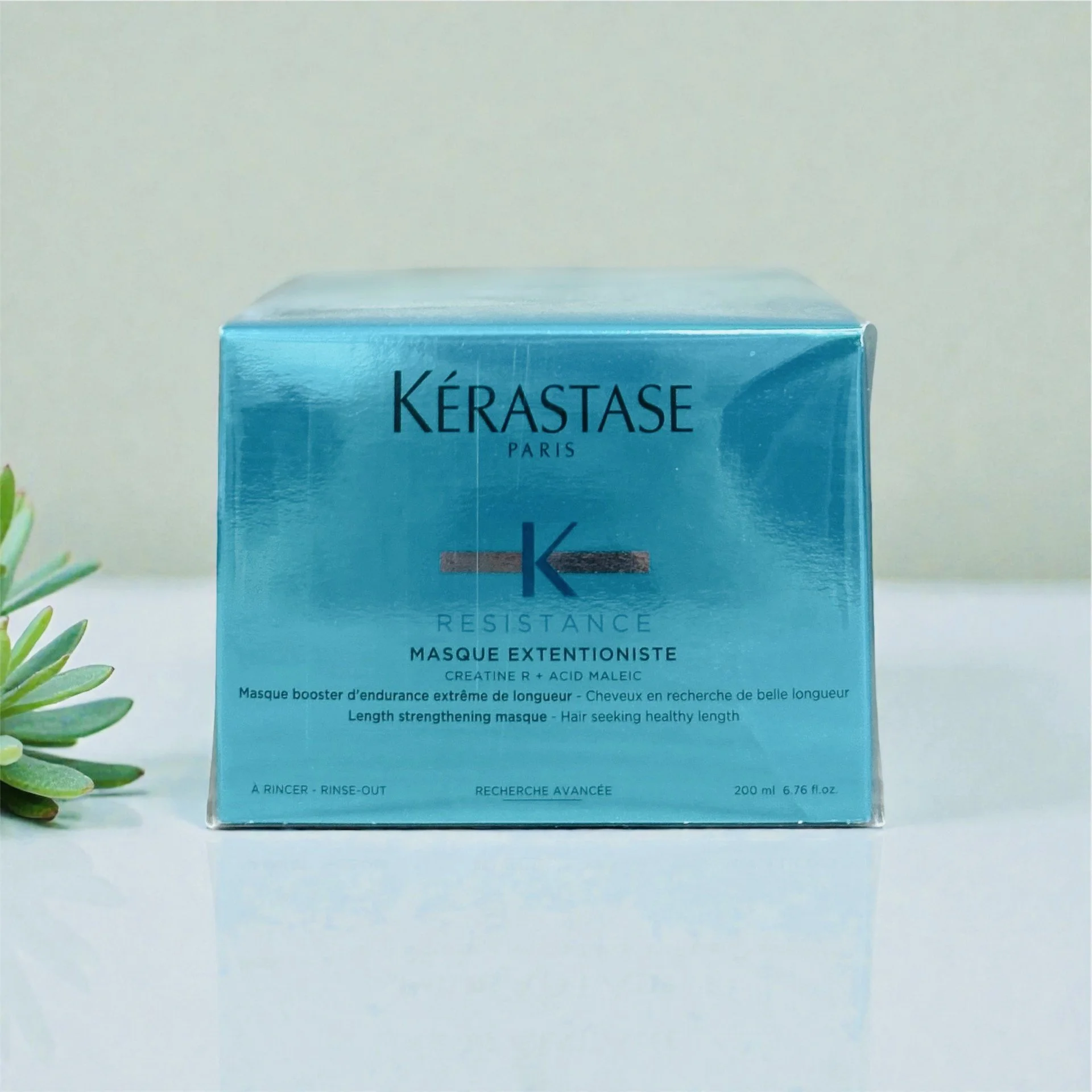 Blue box of Kérastase Resistance Masque Extensioniste hair treatment with a small green plant on the left, against a light background.