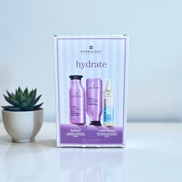 Pureology hydrate and color fanatic hair care products on a shelf next to a small potted succulent plant.