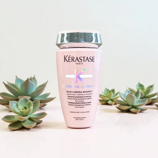 Pink bottle of Kerastase Chroma Respect shampoo with succulents on a white background.