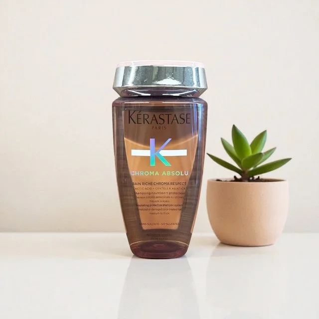A bottle of Kerastase Chroma Absolu hair shampoo next to a small potted succulent plant on a white surface