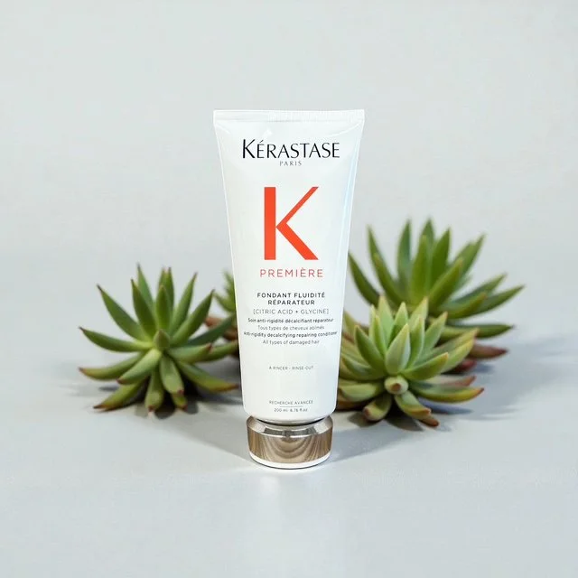 Kérastase Paris Premieré repairing anti-damage conditioner in a white tube with a silver cap, placed in front of green succulent plants.