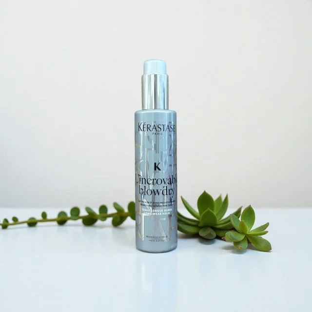 A bottle of Kerastase Incroyable Blowdry hair styling product with a succulent plant nearby on a white surface against a white background.