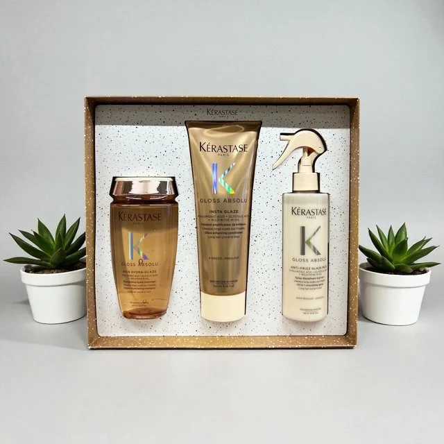 Set of three Kerastase hair care products in a gift box, flanked by two small potted succulent plants on a light-colored surface.