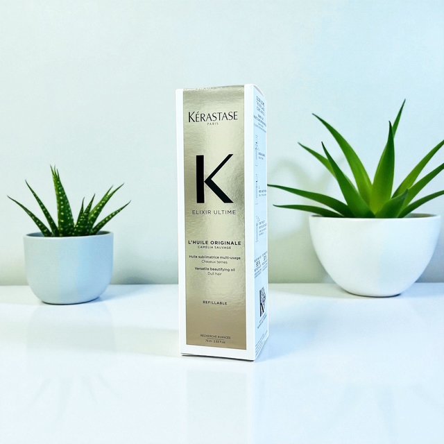 Kérastase Elixir Ultime hair oil bottle between two potted succulents on a white surface.