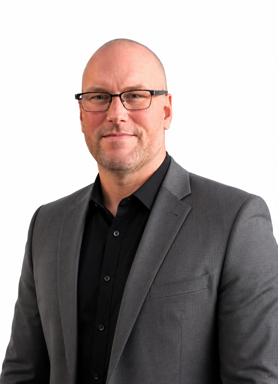 Professional headshot of a bald man with glasses, wearing a gray suit jacket and black shirt, smiling against a white background.
