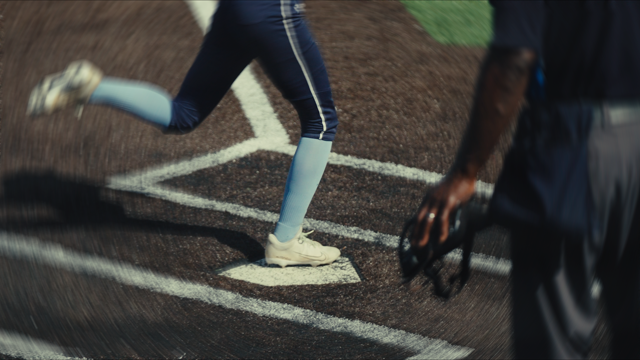 A softball players runs to home plate and steps on the plate as she scores her run. The umpire's leg next to home plate.
