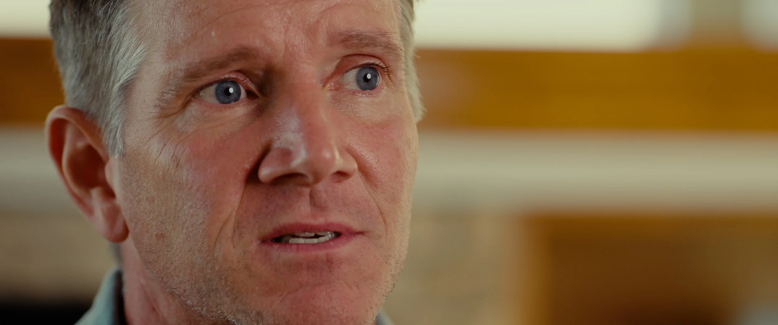 Close-up of an older man with blue eyes and gray hair, looking to the side with a neutral expression.