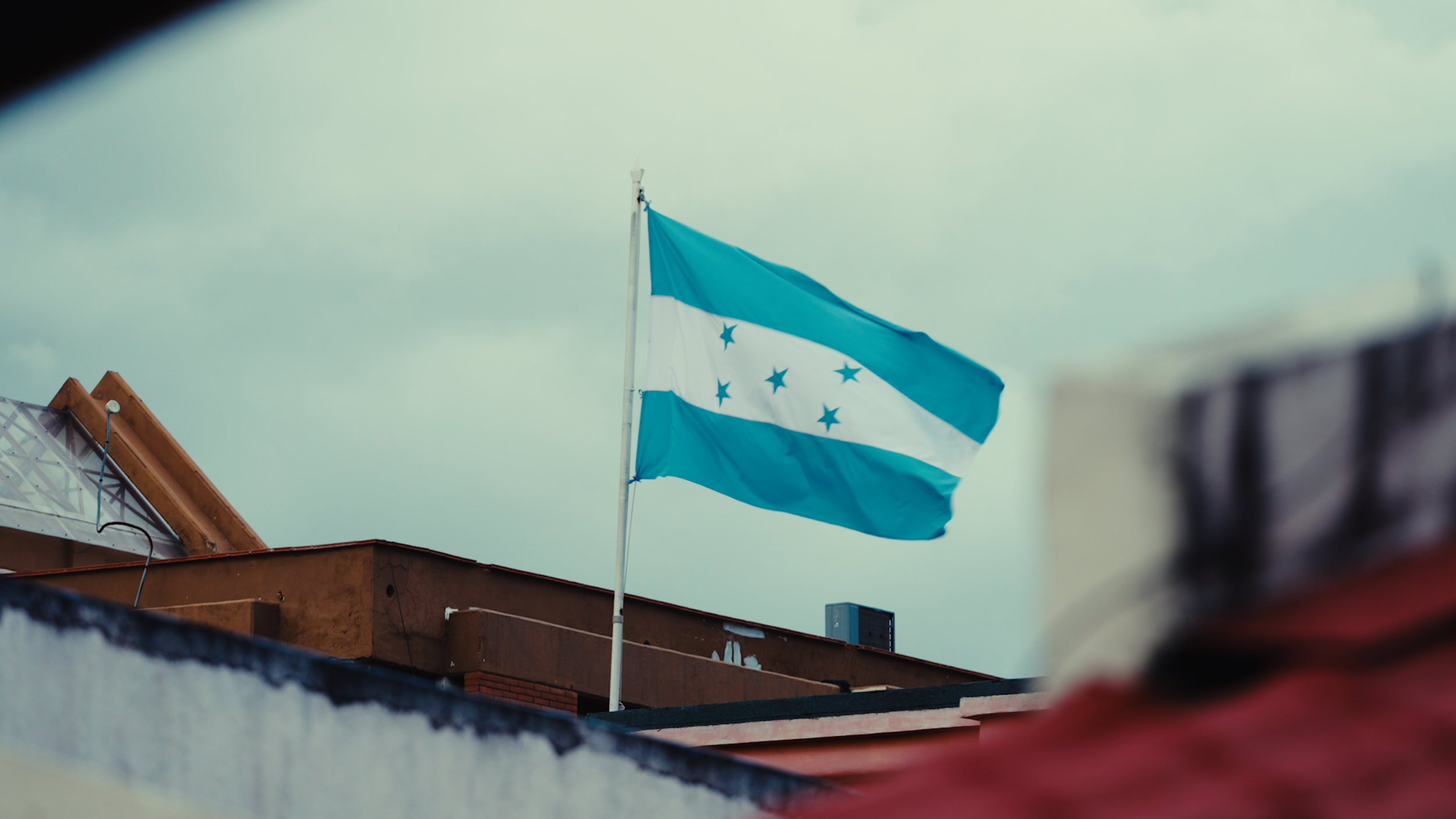 Honduran flag waving in the wind on top of a building with a cloudy sky background.
