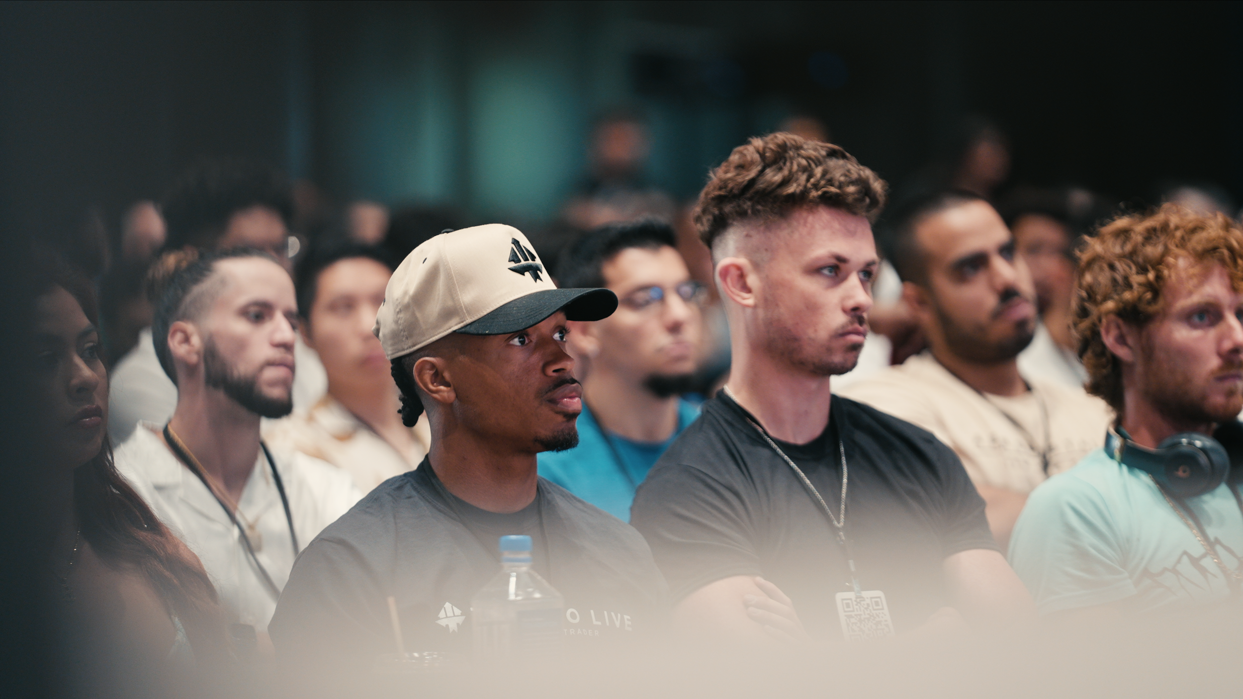A diverse group of people attentively listening at a conference or event, with focused expressions, some wearing headphones.