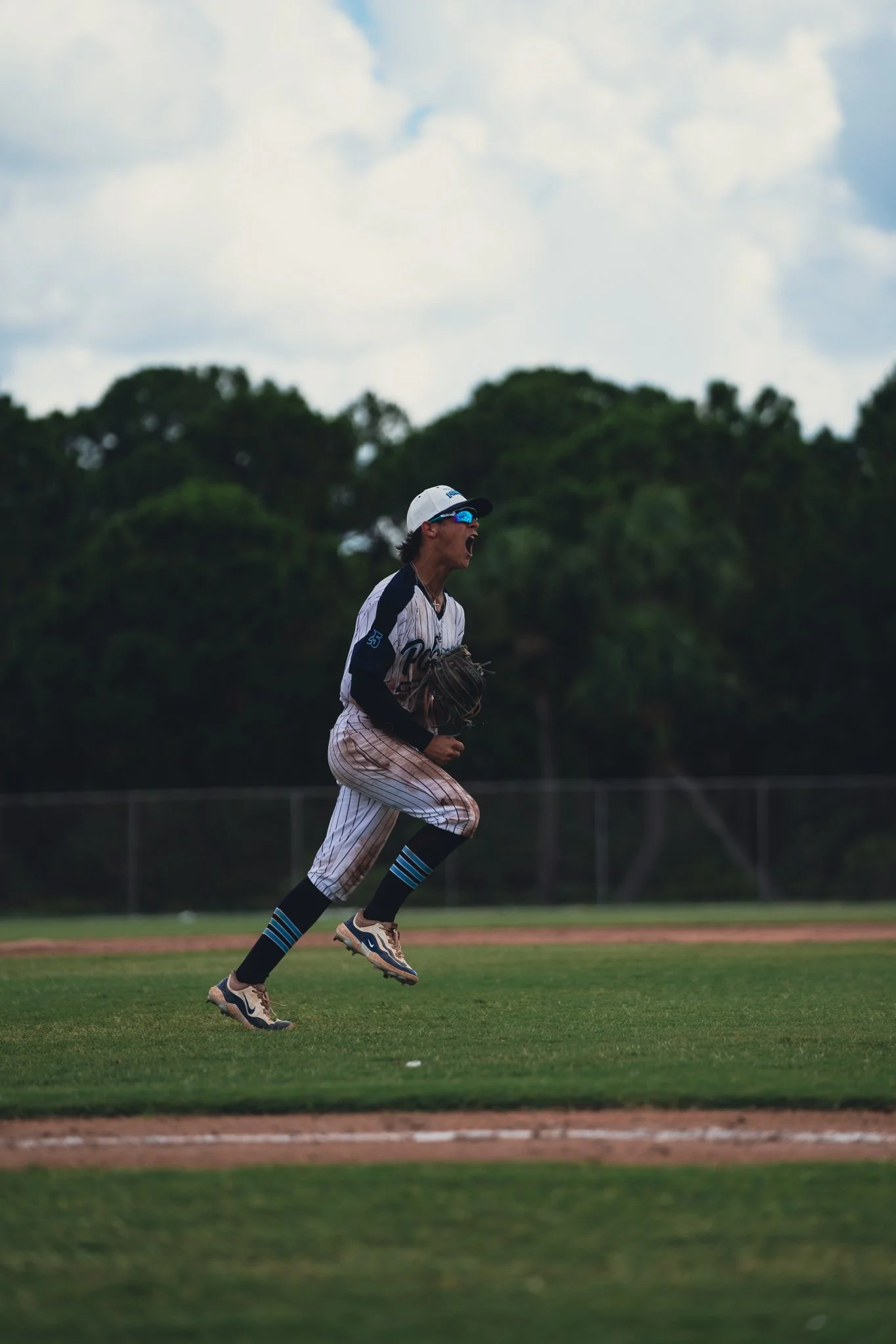 A baseball player running on the field during a game, wearing a striped uniform, baseball gloves, and sunglasses.