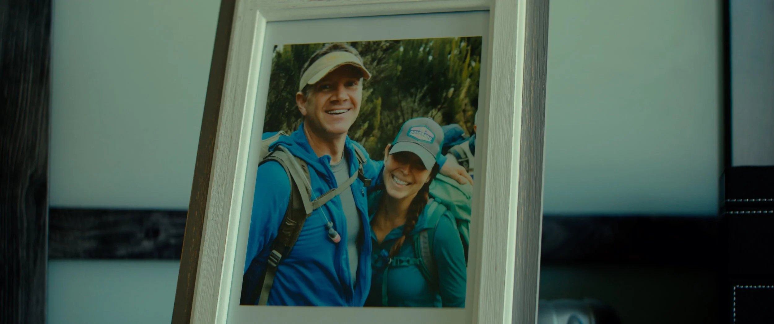 Framed photograph of a smiling man and woman dressed in outdoor hiking gear, standing outdoors with trees in the background.