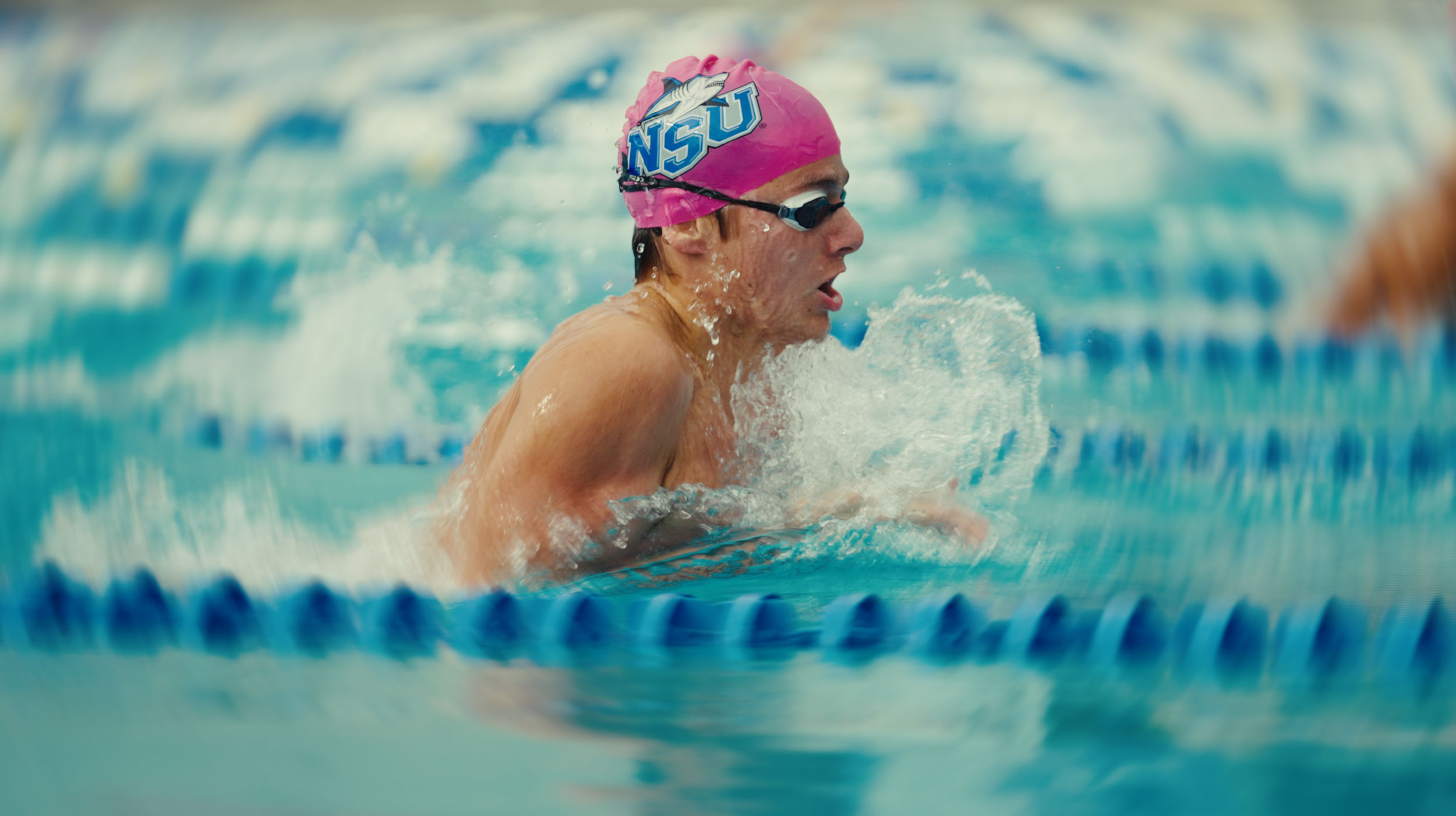 Swimmer in a pink swim cap and goggles swimming in a pool.