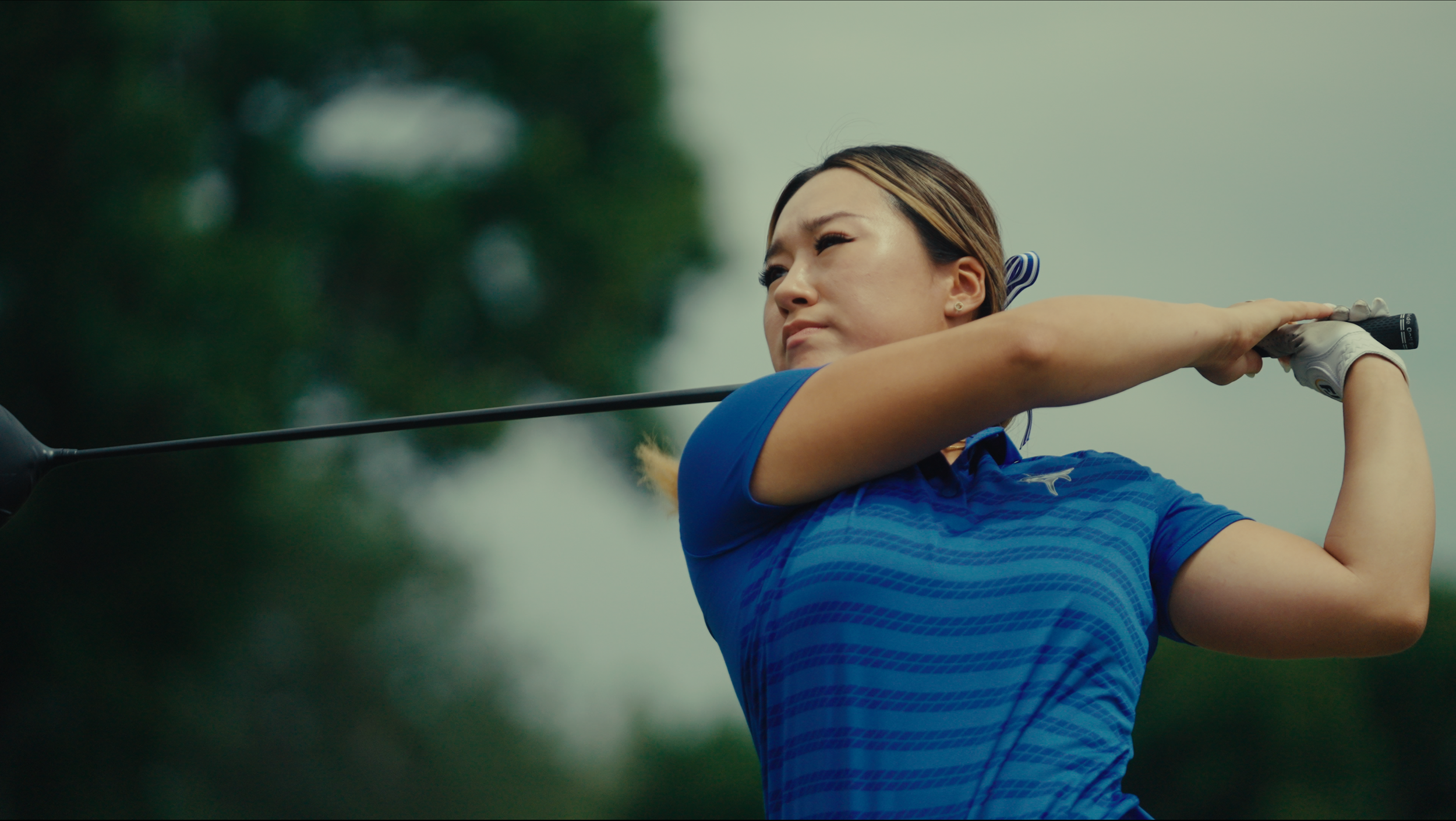 Female golfer in blue shirt swing shot on golf course.