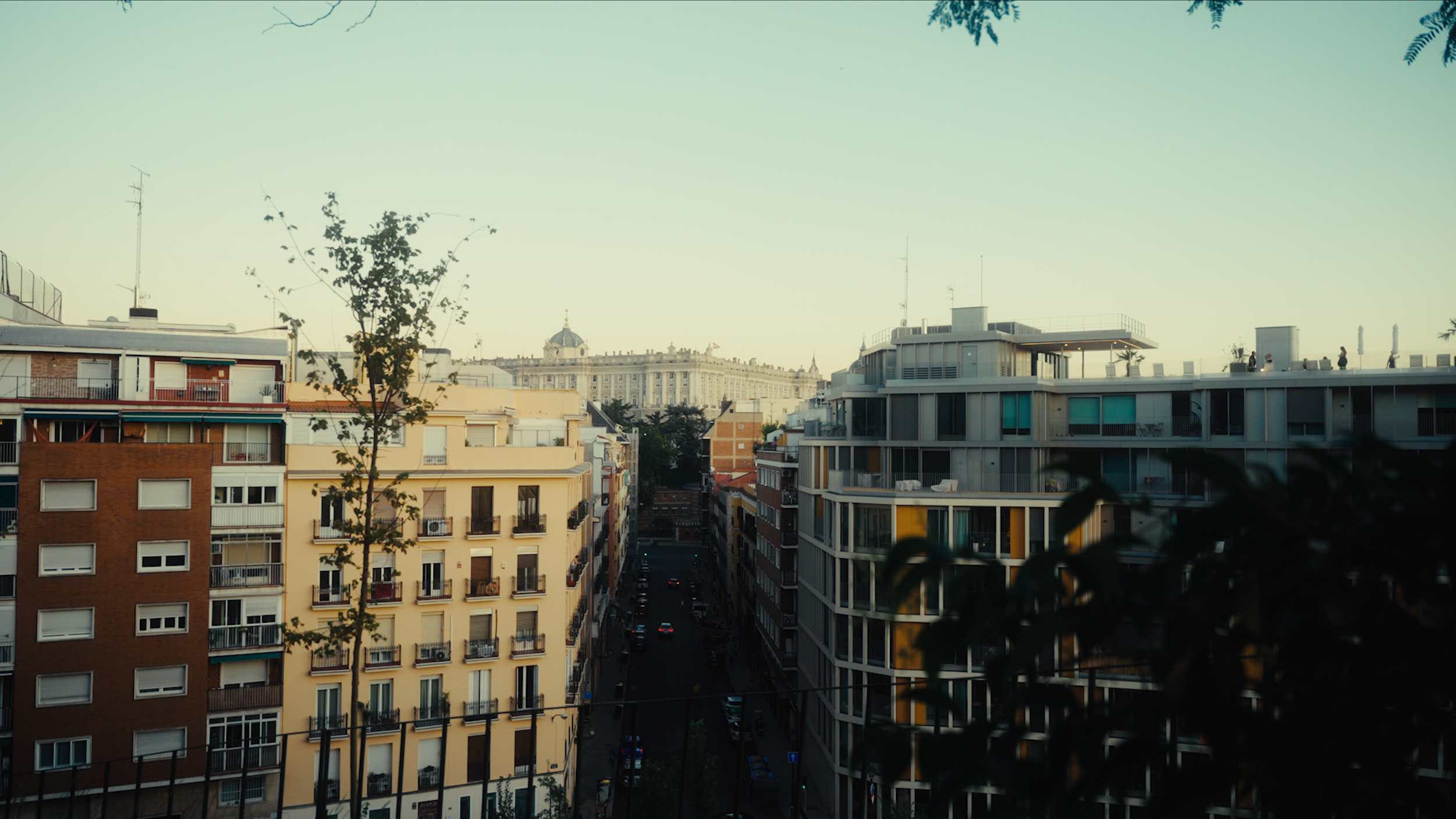 Cityscape with apartment buildings, a street, and a historic building in the background under a clear sky.