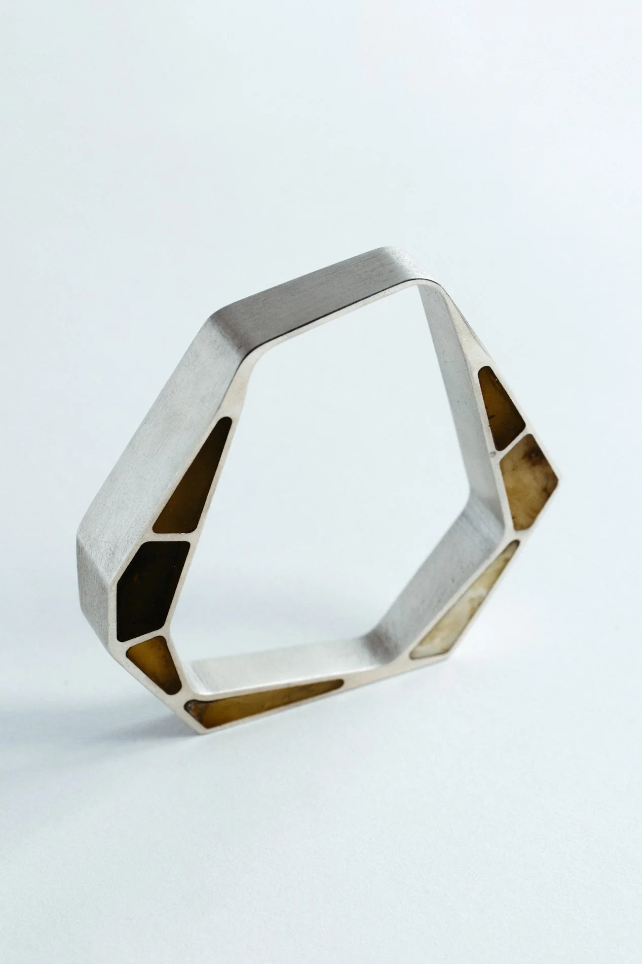 Engrenages bracelet V1.1 by Sajfrt — closed interlocking form in silver or gold with amber stone. Handcrafted in Belgium with architectural intent.