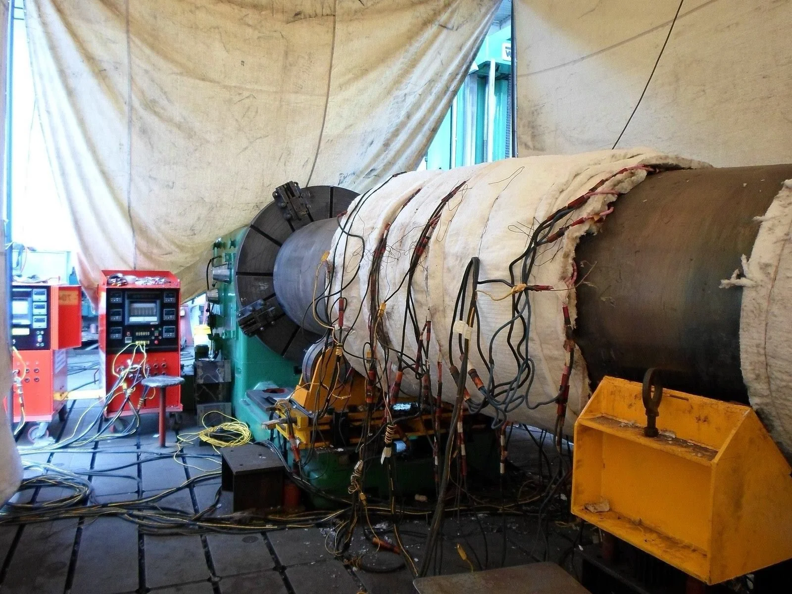 Un gran tubo de ensayo de agua geotérmica con cables eléctricos conectados a un equipo de medición y control en un ambiente de laboratorio.