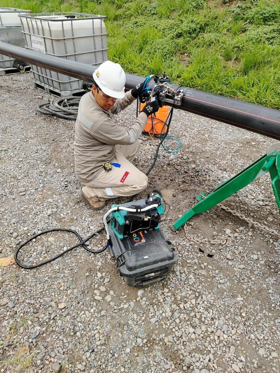 Técnico trabajando en una tubería negra en una zona exterior con césped y graba en el suelo con equipo especializado.