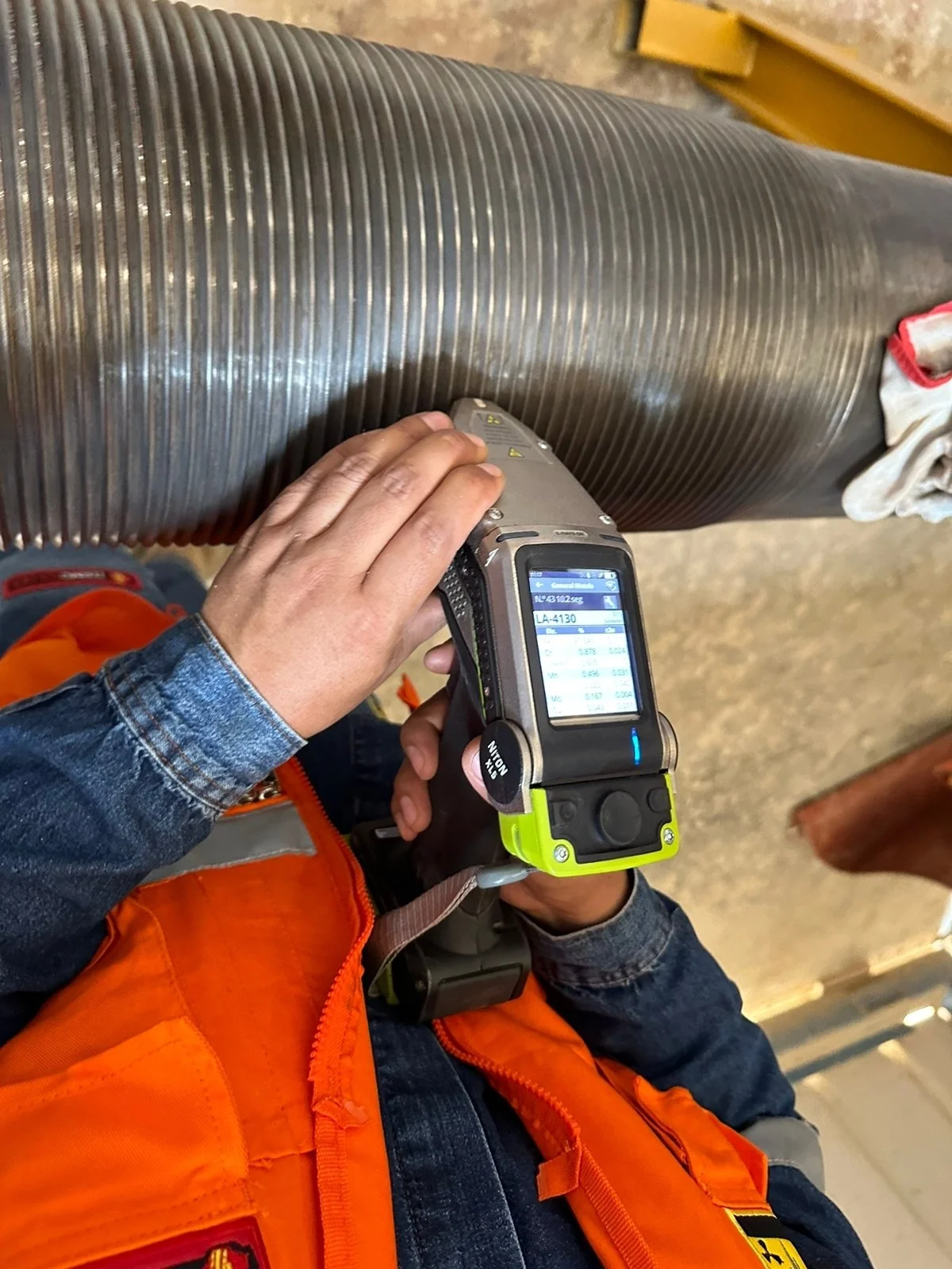Persona usando un escáner de calidad para inspeccionar una tubería grande de metal en un entorno industrial.