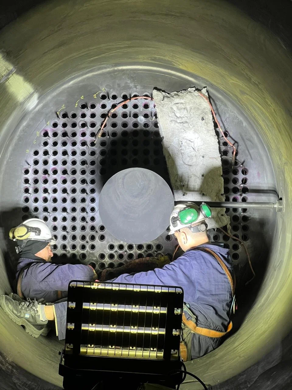 Dos trabajadores con casco y equipo de protección dentro de un gran tanque, realizando mantenimiento o inspección en sus partes internas.