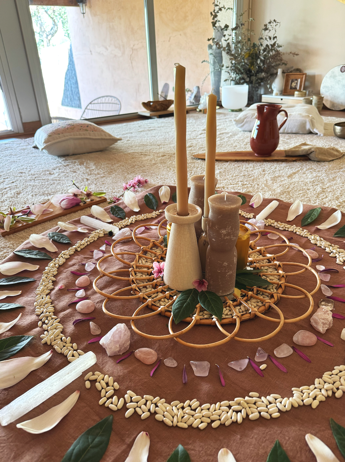 Configuración de altar con velas, flores, cristales y cartas, en un círculo en una alfombra beige.