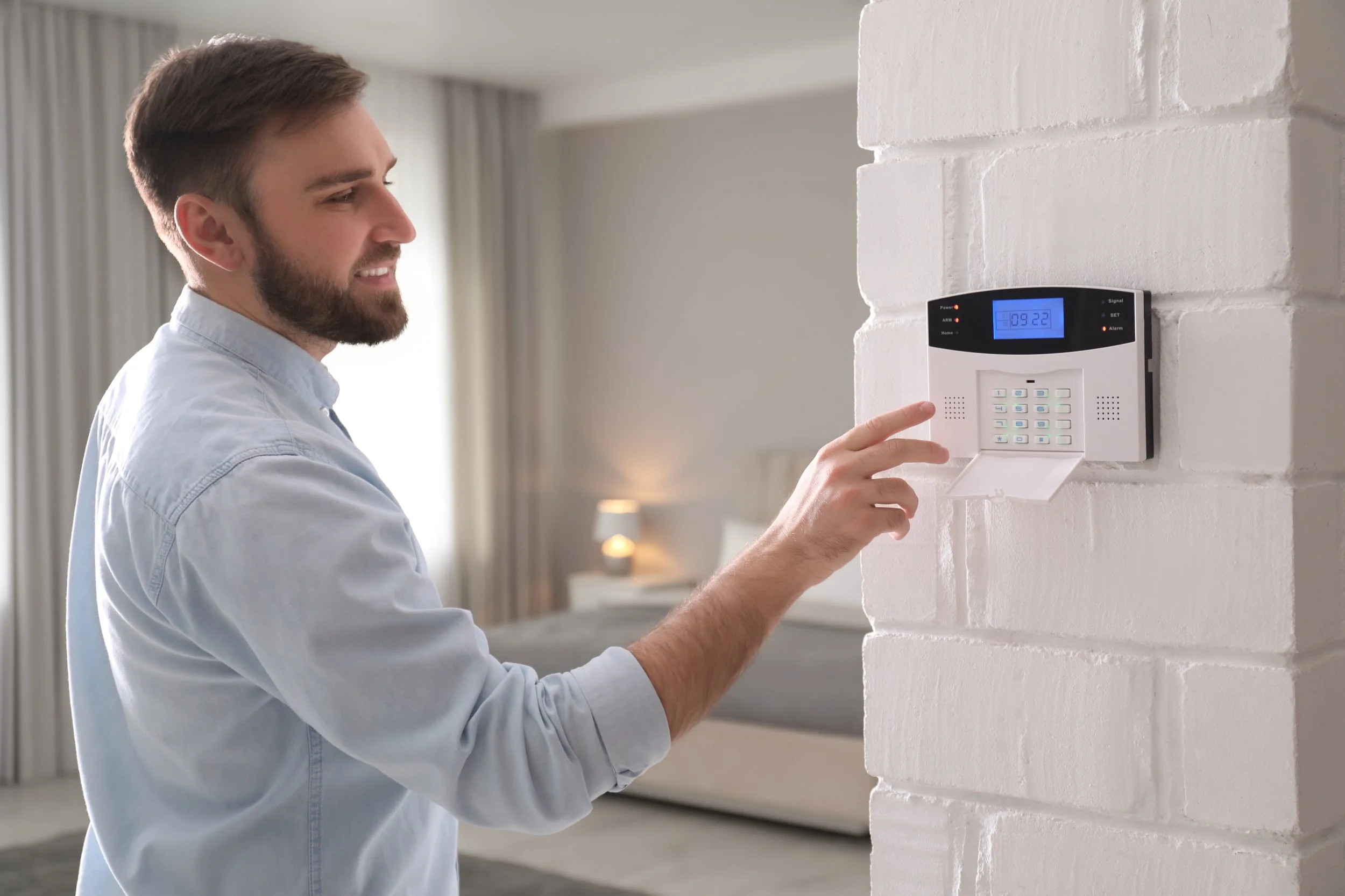 Man using a security keypad mounted on a white brick wall in a bedroom.