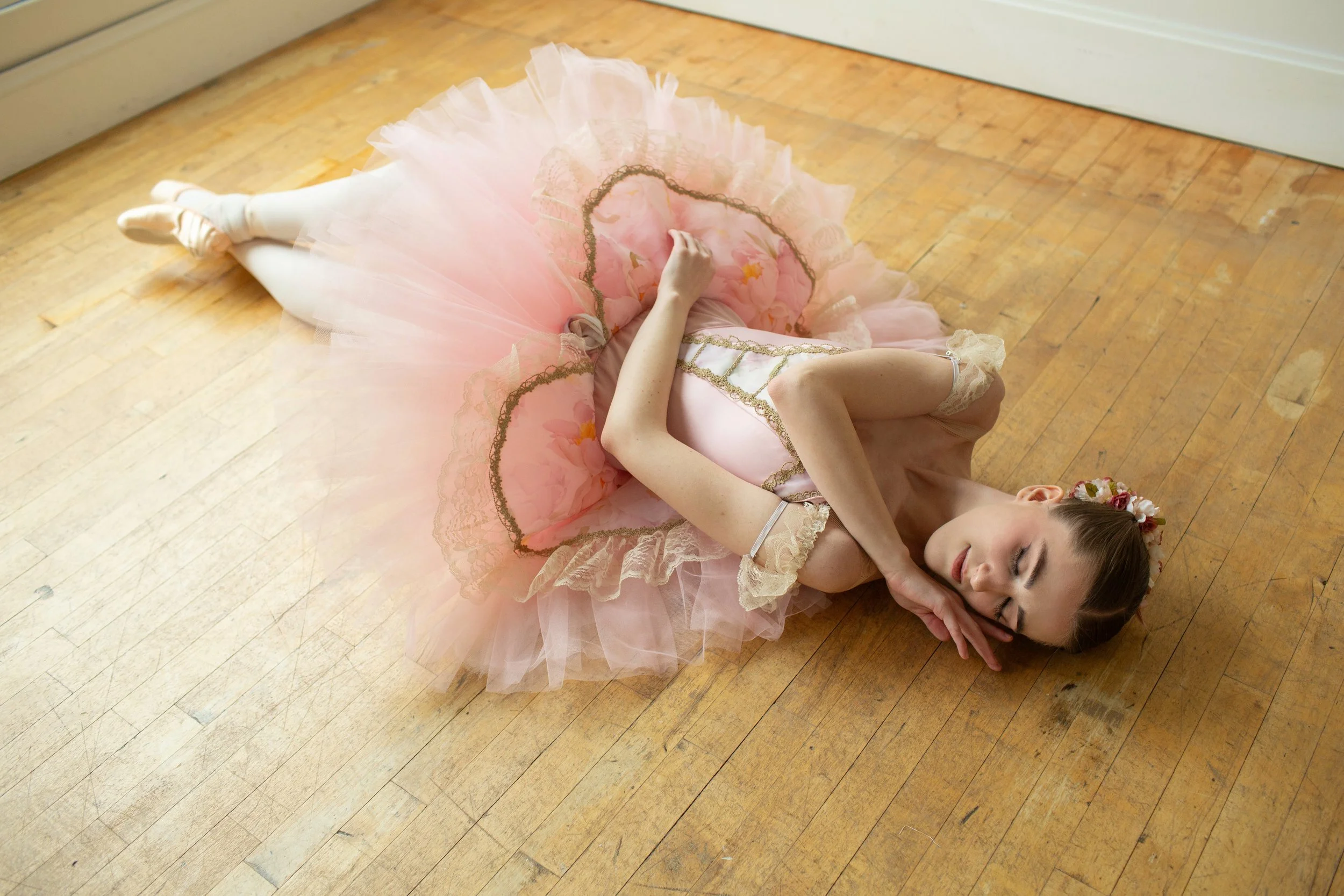 Professional ballerina posing in an intricate pink bodice and floral tutu with a split plate. Tutu showcases qualities often seen in costumes worn during professional ballets such as Sleeping Beauty. 