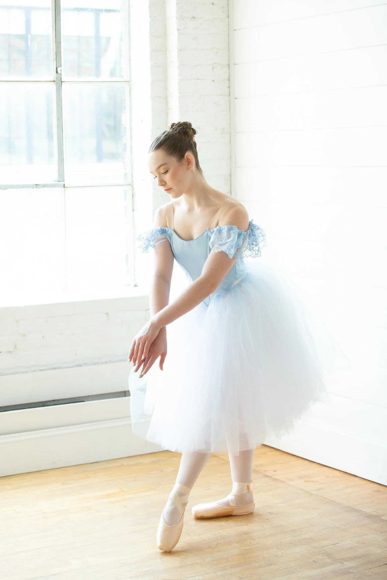 Model during the annual photo event posing in a white and light blue romantic tutu featuring a fitted blue bodice and lace drape sleeves. 