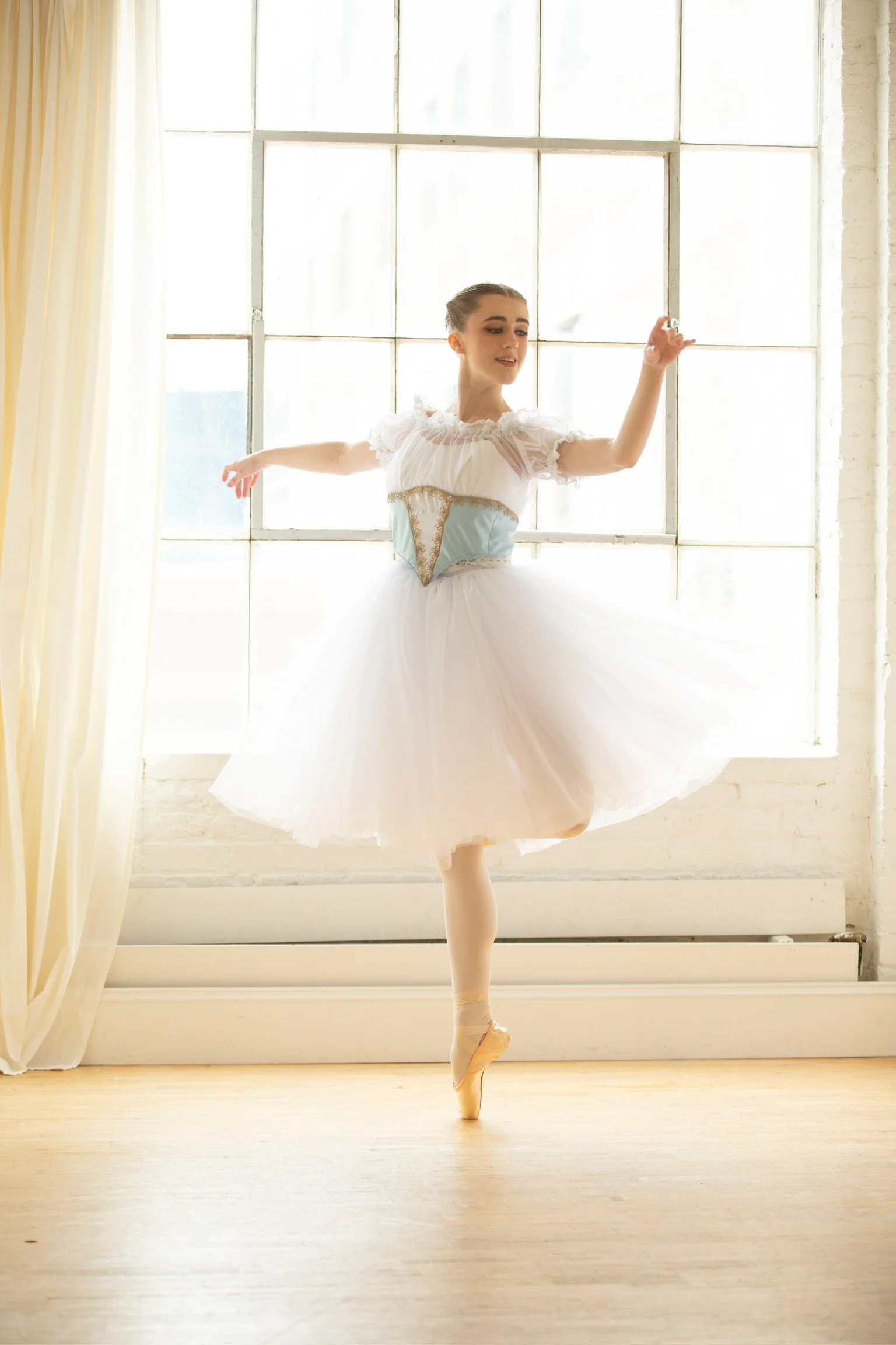 Professional ballerina dancing the Giselle ballet in a white romantic tutu and blue floral peasant bodice with a chemise. 