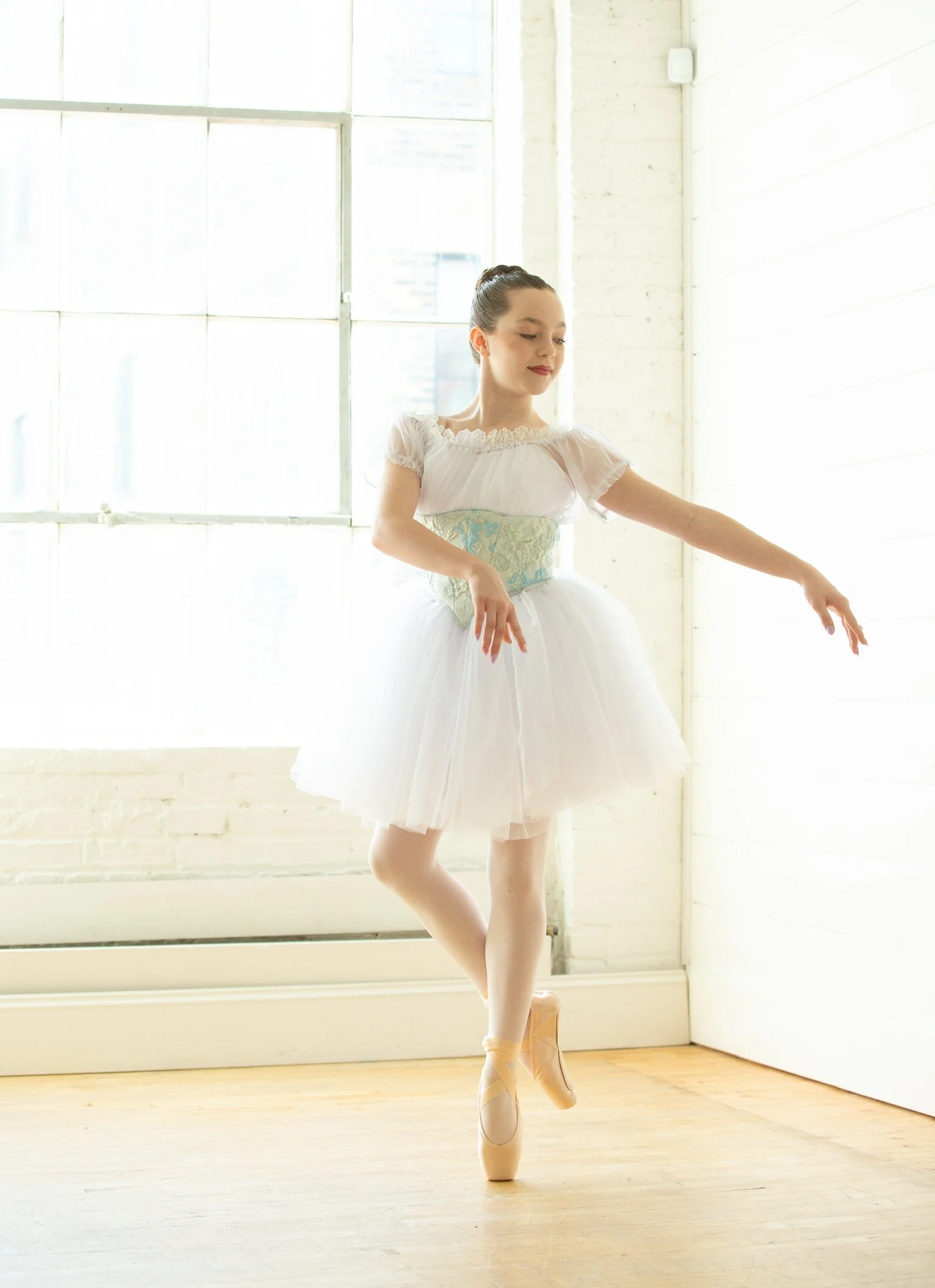 A young ballet student models during the annual photo event dancing in a short white romantic-styled bell tutu shape, peasant bodice, and white chemise. 