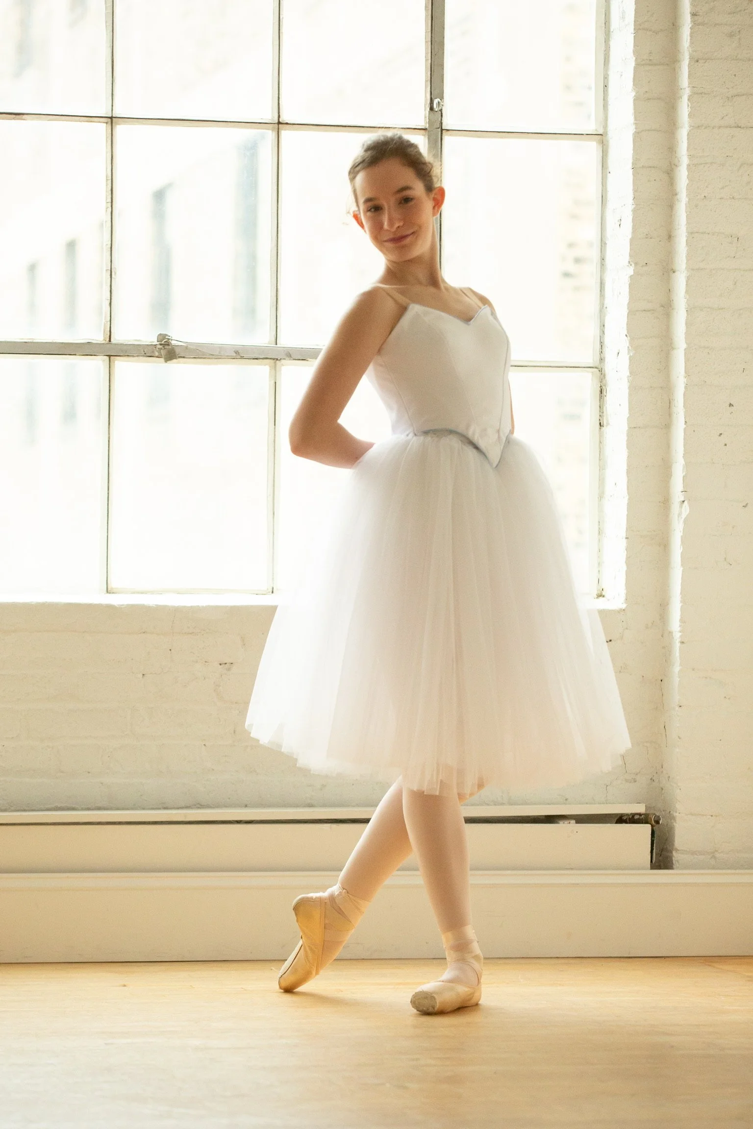 Ballet student wearing a simple white classical romantic tutu that emulates corps de ballet pieces such as snow. Costume designed by Le Chaton Tutus. 