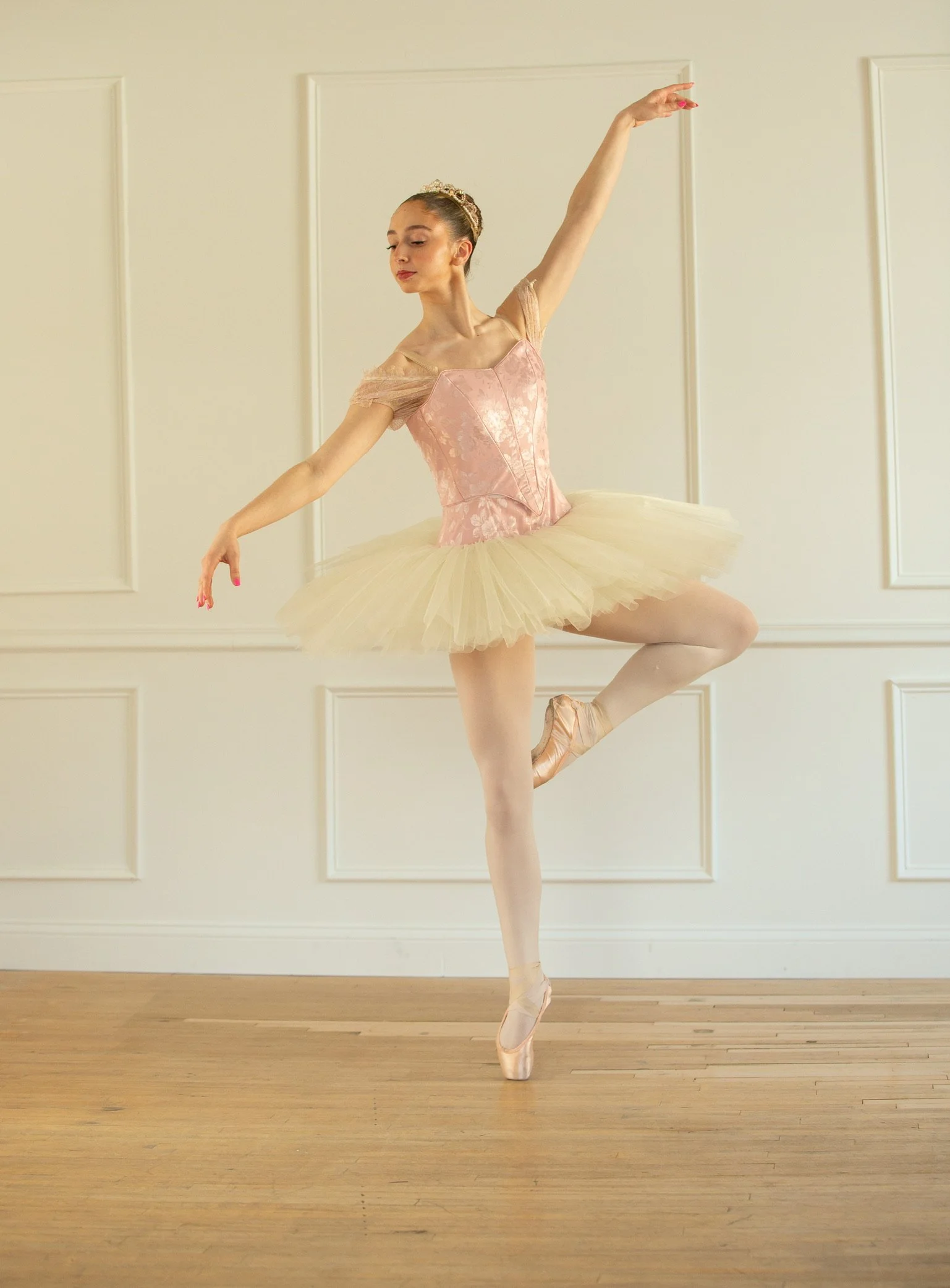 Professional ballerina wearing a pink longline bodice and a pleated ivory classical tutu while rehearsing in-studio.
