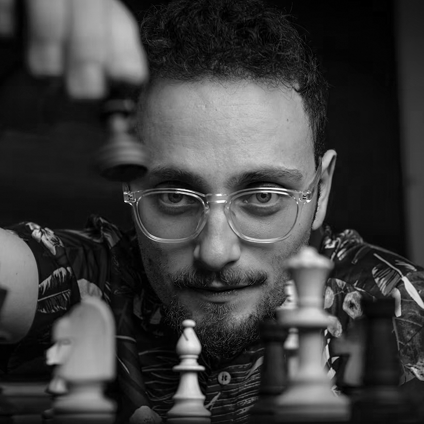 Black and white photo of a Levy Rozman with glasses focusing intently on a chessboard.